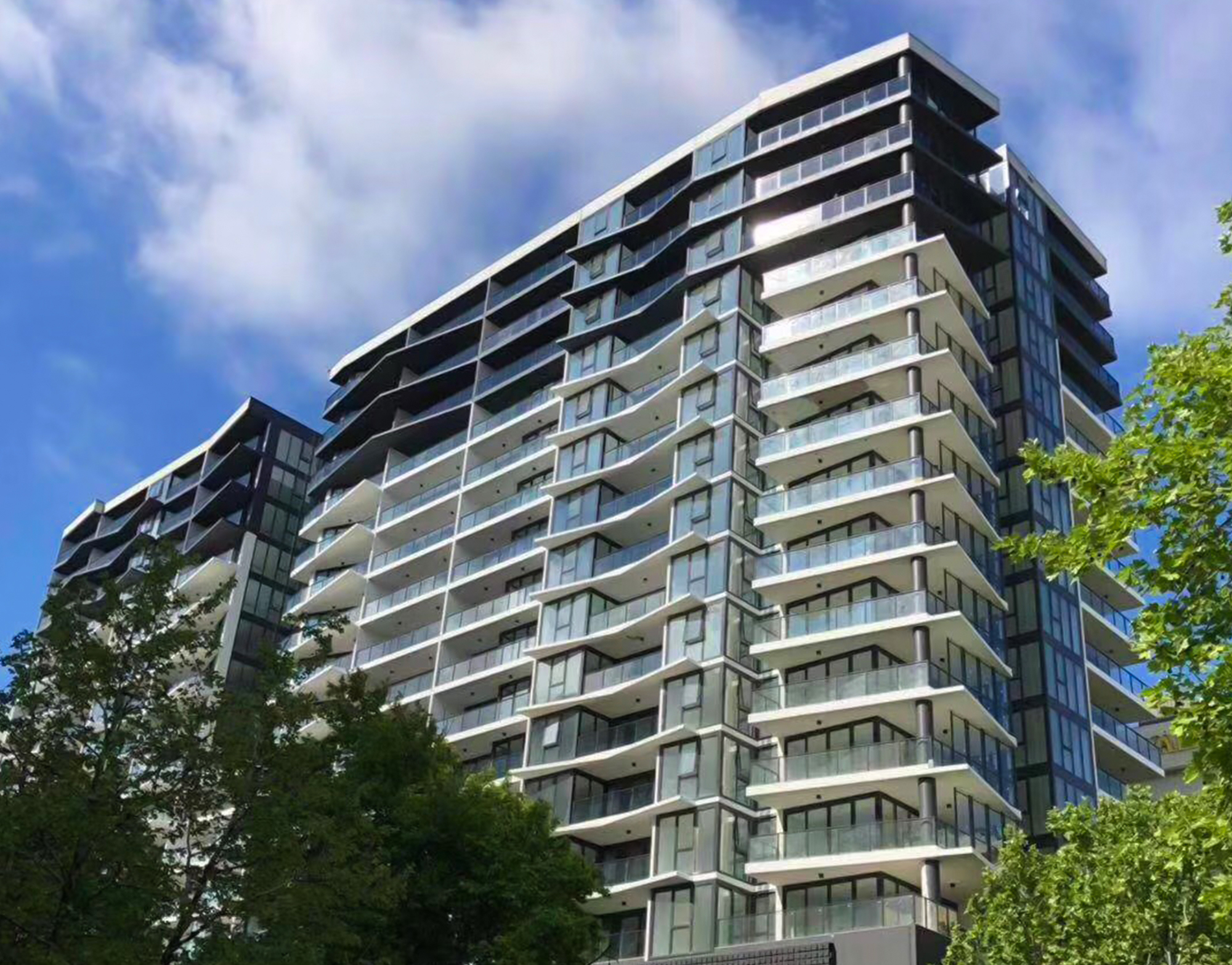 Completed residential tower with stacked grey balconies and full-height glazing seen from the street