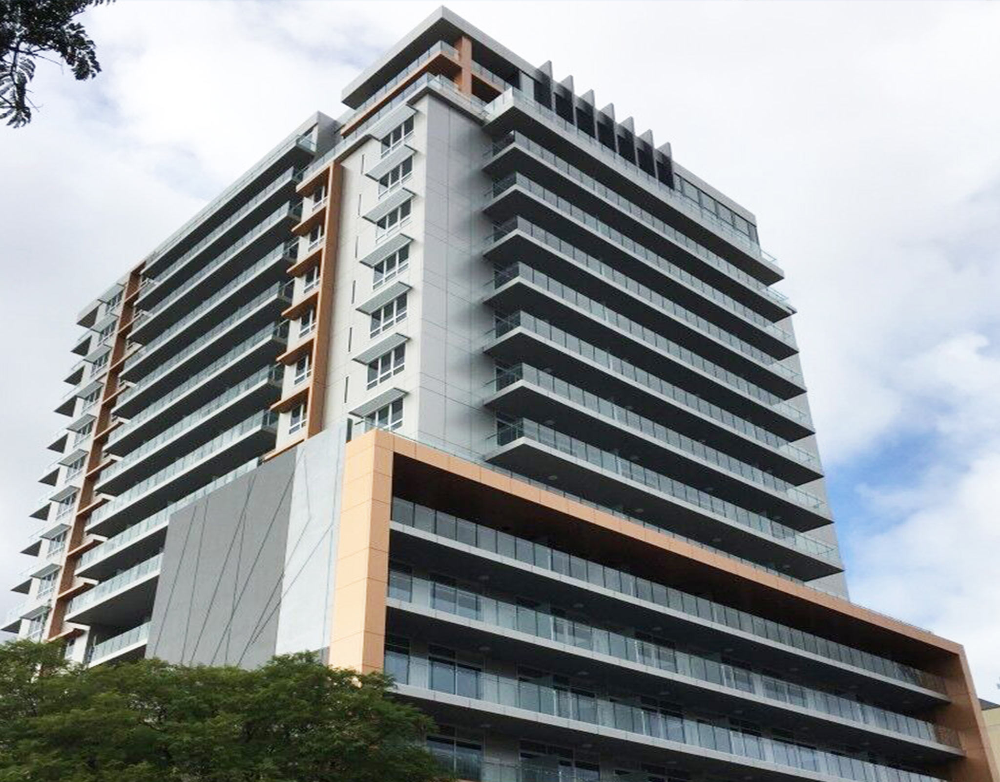 Completed hotel tower with white balcony bands and a timber-clad podium volume