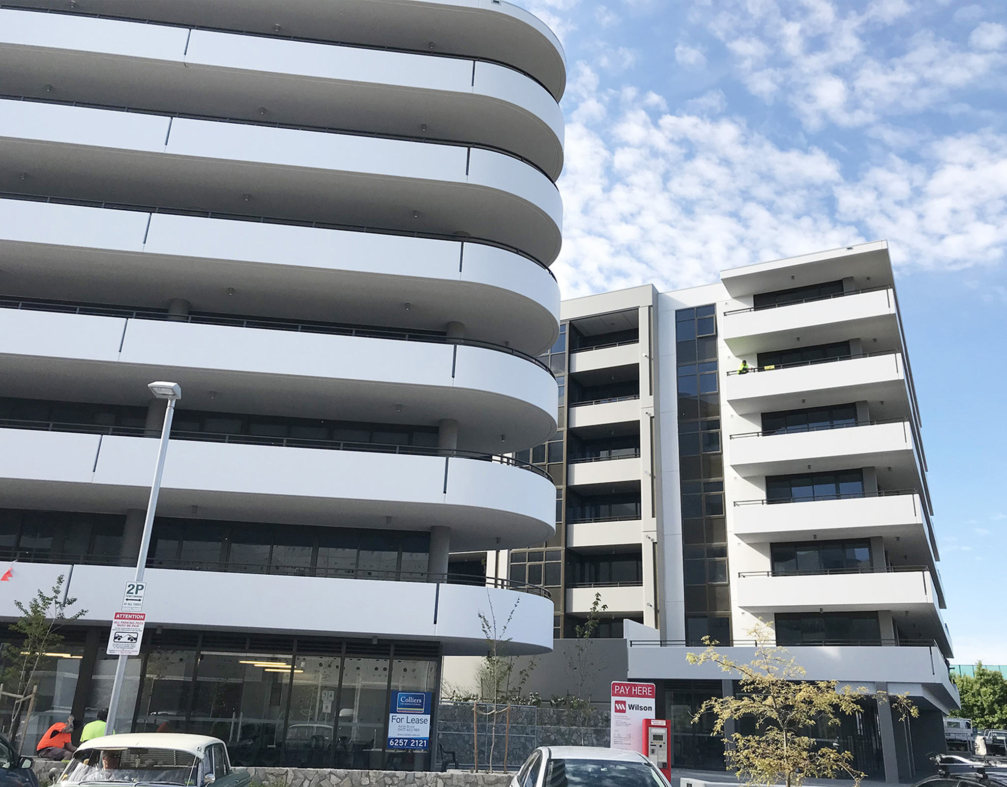 Curved white residential facade with continuous balcony bands above a glazed retail base