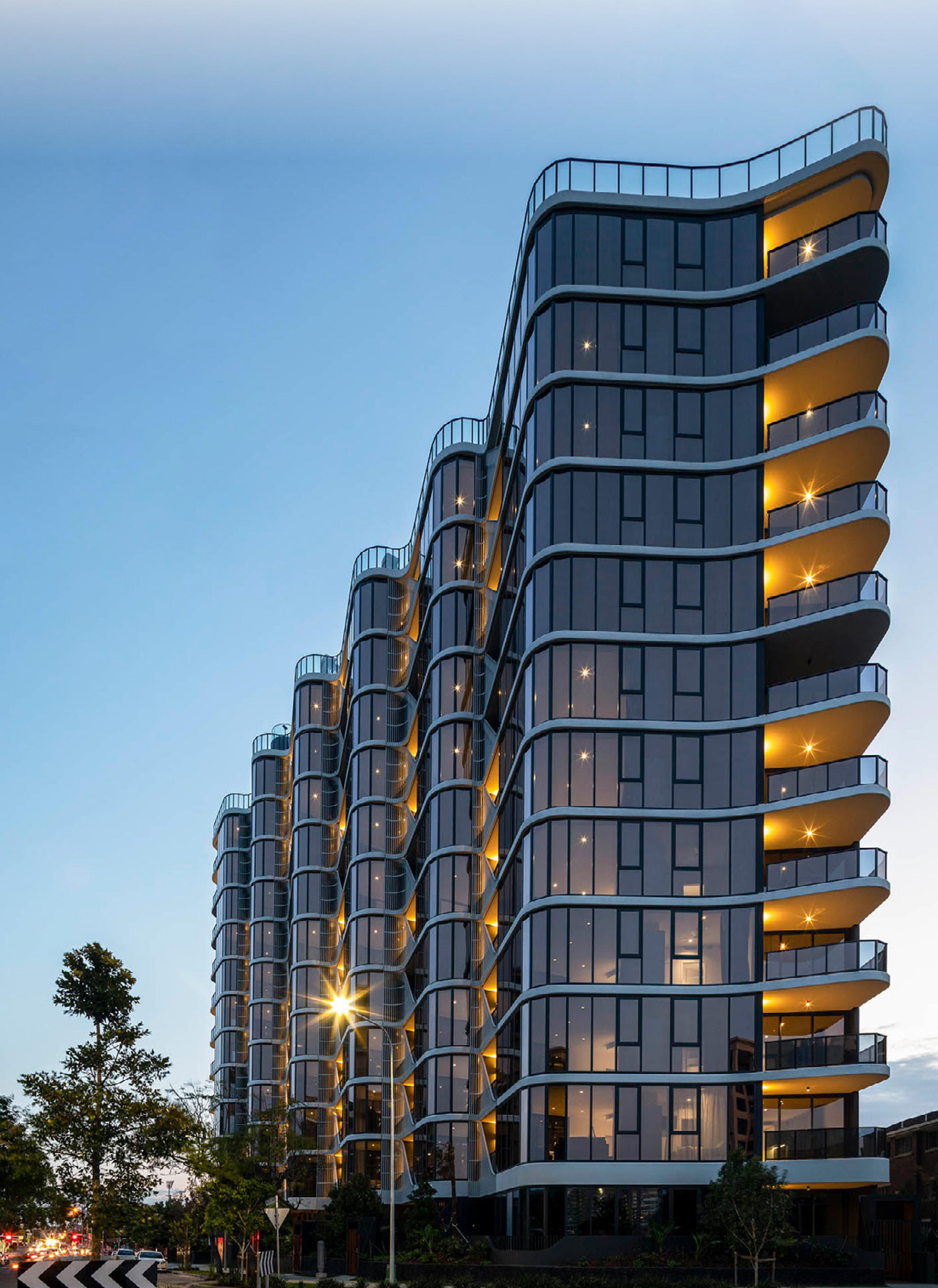 Dusk rendering of a curved residential tower with warmly lit balconies