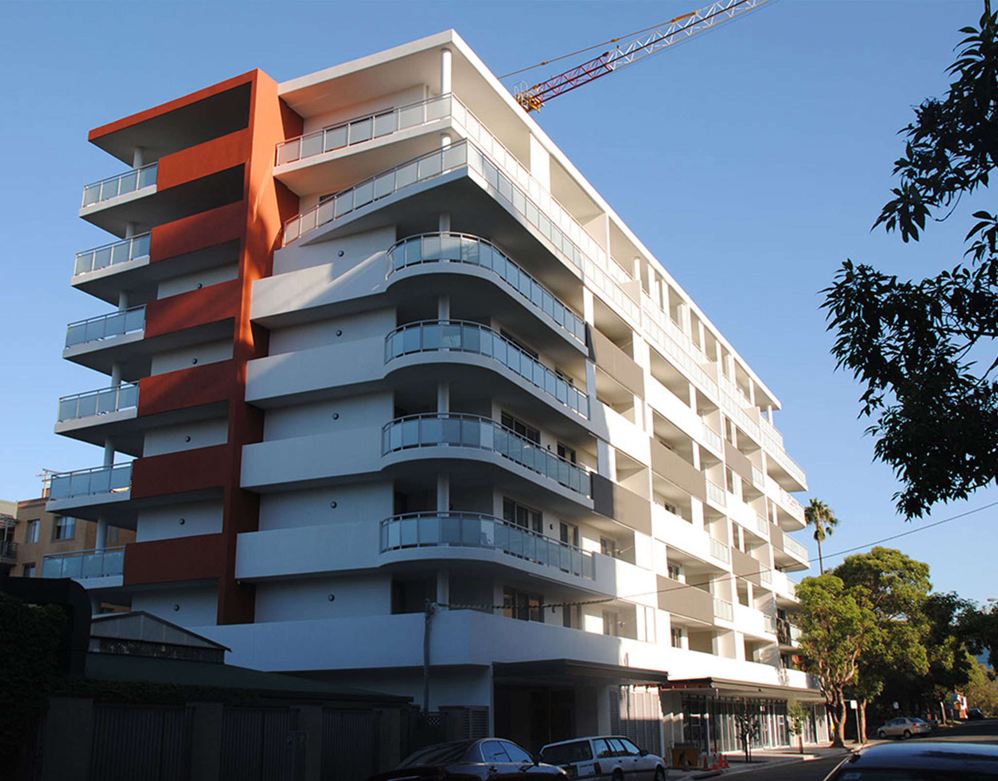 Completed mid-rise apartment building with a red accent volume and continuous balcony glazing